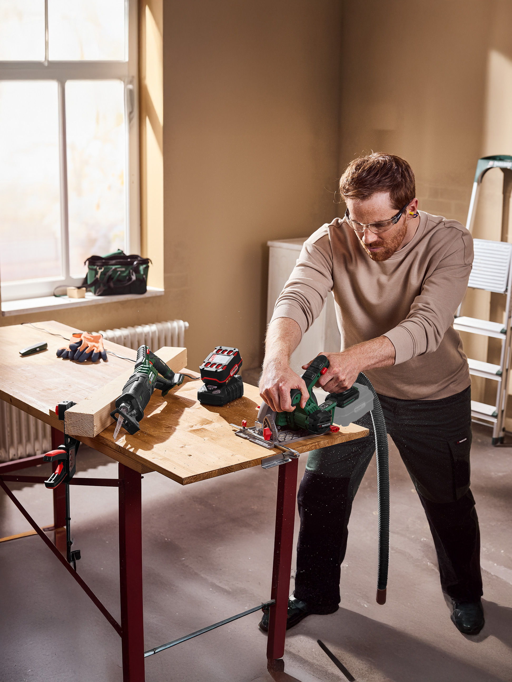 Een man gebruikt een cirkelzaag om hout te zagen op een werkbank, met een reciprozaag in de buurt.