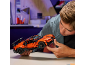 Een jonge man zet aan een tafel een oranje speelgoedsportwagen van bouwstenen in elkaar.