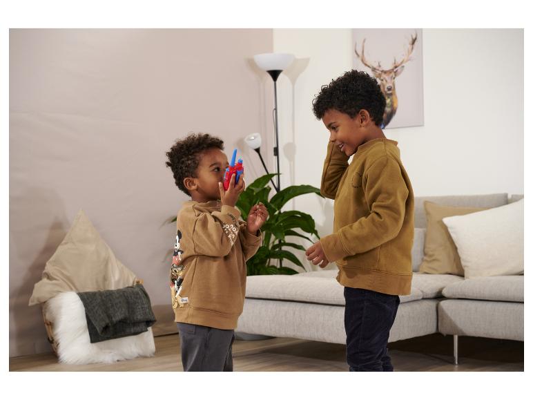 Twee jongens in bruine sweatshirts spelen met een walkie-talkie in een woonkamer.