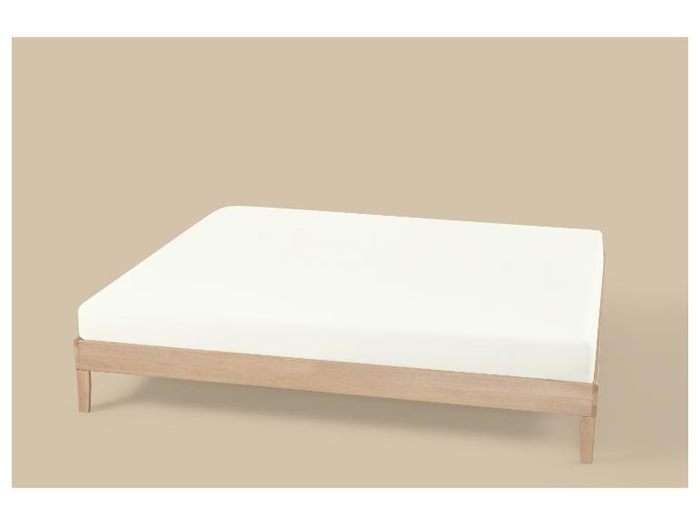 Licht houten bedframe met een wit matras op een beige achtergrond.