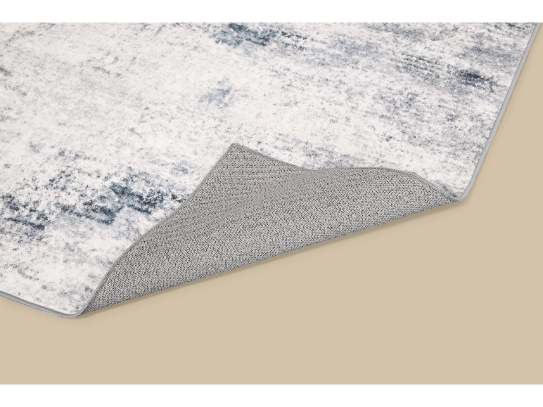 Grijs en wit abstract patroon vloerkleed met een omgevouwen hoek, die de getextureerde onderkant onthult.
