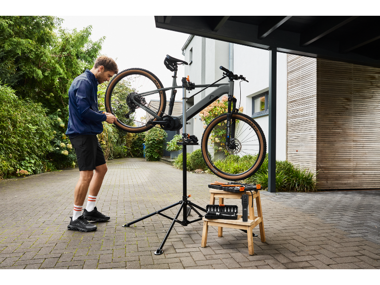 Man repareert elektrische mountainbike op reparatiestandaard met gereedschap ernaast.