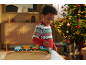 Lachend kind speelt met houten trein, verlichte kerstboom op de achtergrond.