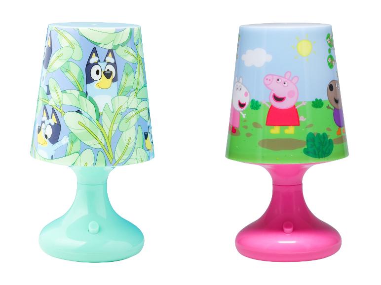 Twee kinder tafellampen: één met blauwe hondenfiguren en groene bladeren, de andere met varkensfiguren in een veld.