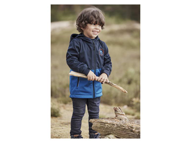 Een jongetje draagt een blauwe softshell jas met een capuchon en een print van 'Arctic Adventure'