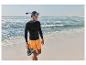 Man in zwart shirt, oranje korte broek, snorkelmasker en waterschoenen op het strand.