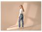 Blonde vrouw in jeans en witte top met lange mouwen, kijkt over haar schouder.