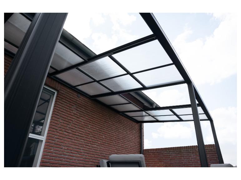 Terrasoverkapping met een transparant dak en zwart frame bevestigd aan een bakstenen muur.