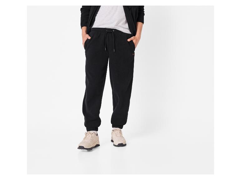 Man in zwarte joggingbroek, grijs T-shirt en zwarte hoodie met beige sneakers.