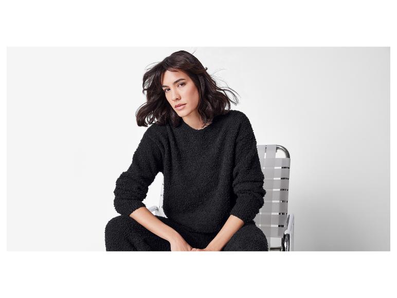 Een vrouw in een zwarte pluizige trui en broek zit op een stoel.