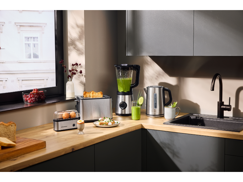 Keukenontbijtset: broodrooster, blender, waterkoker, eierkoker en vers eten op houten aanrecht.