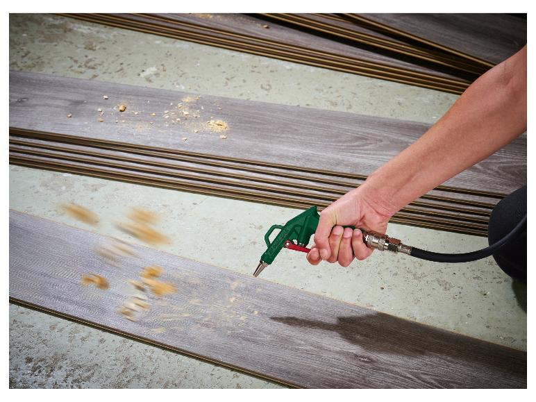 Een persoon gebruikt een luchtblaaspistool om zaagsel van een laminaatplank te verwijderen.