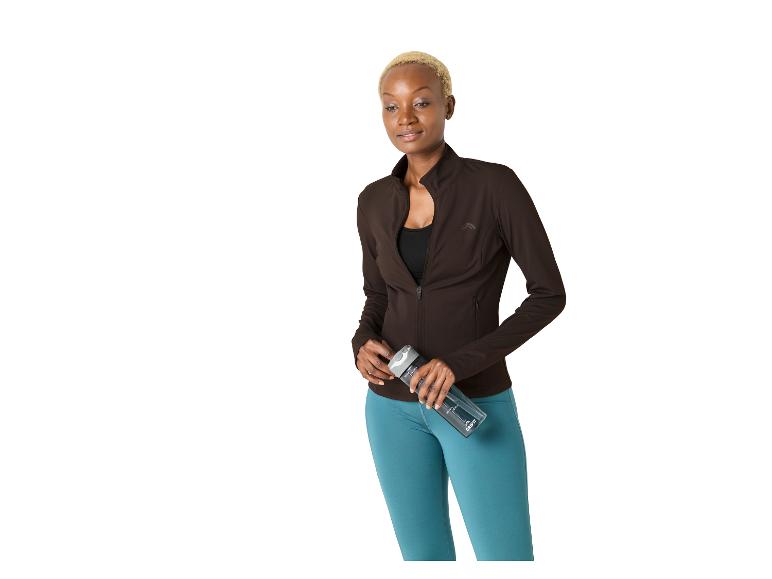 Vrouw met kort haar, bruin sportjack en blauwe legging, met een waterfles.