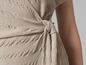 Close-up van een beige getailleerde jurk met een strik.
