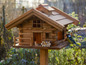 Een houten vogelhuisje in chalet-stijl met een blauwe vogel erop