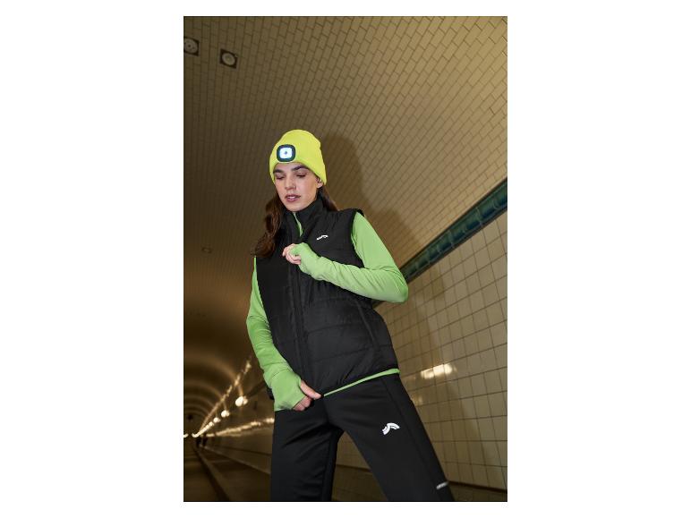 Vrouw in zwart vest, groen shirt en gele muts met licht in een tunnel.