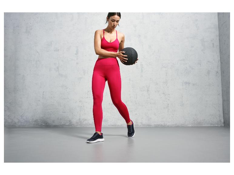 Een vrouw in roze sportkleding met een zwarte trainingsbal.