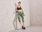 Vrouw in groene sportlegging en zwarte sportschoenen met springtouw.