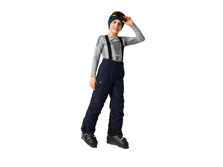 Jongen in ski-uitrusting, met een marineblauwe broek, een grijs shirt en skibril.