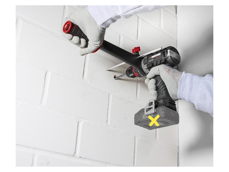 Persoon boort een gat in de muur met een accuboormachine en stofafzuiger.