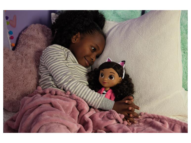 Een jong meisje in gestreepte pyjama knuffelt een pop met kattenoren onder een roze deken.