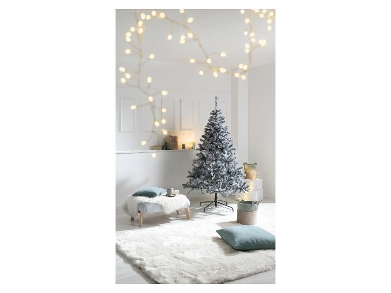 Een bevlokte kerstboom in een witte kamer met lichtslingers en cadeaus.