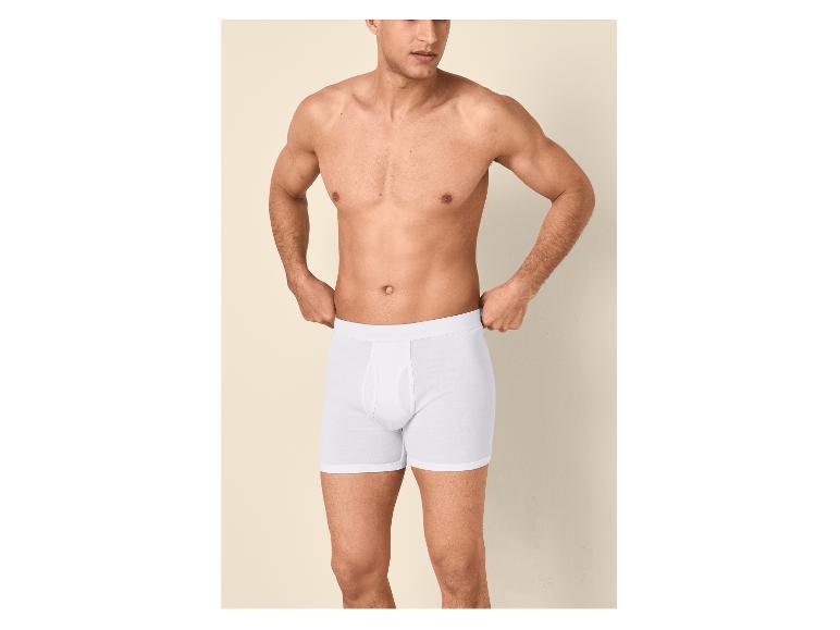 Man zonder shirt in witte boxershorts, die de tailleband aanpast.