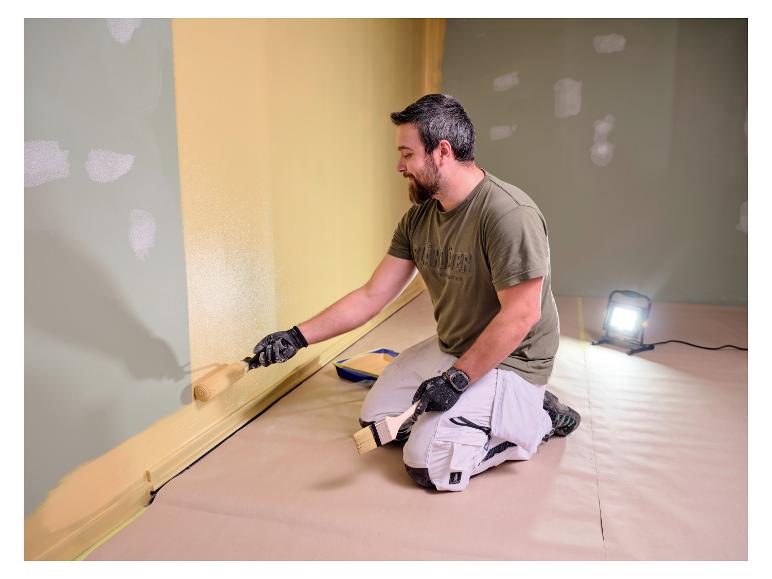 Man schildert muur, verlicht door LIVARNO® werklamp 'The Painter+'.