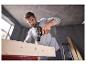 Man met accuboormachine boort in houten plank, met rondvliegend zaagsel.