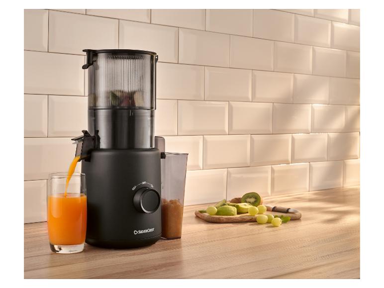 Zwarte sapcentrifuge maakt sinaasappelsap, met vers fruit op tafel.