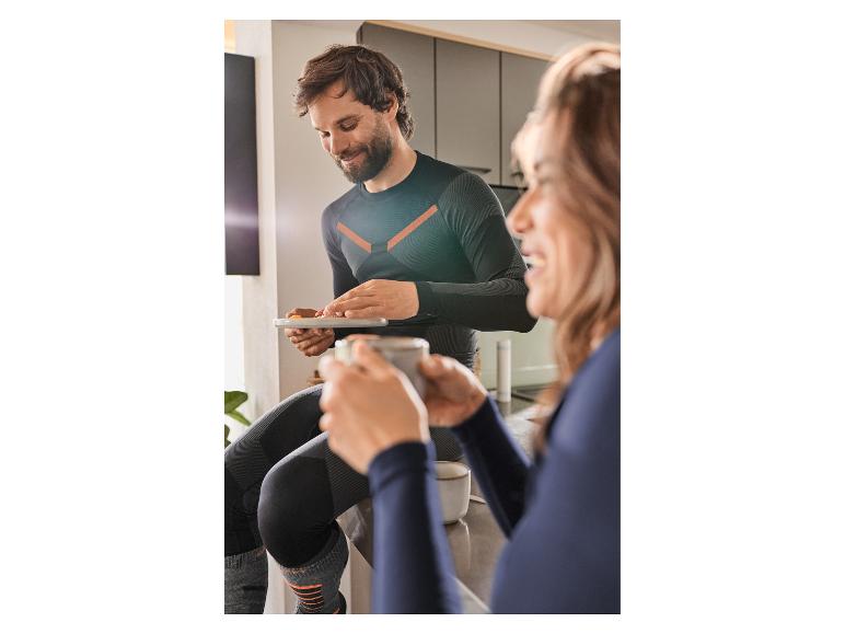 Man en vrouw in sportkleding, man houdt een tablet vast, vrouw drinkt uit een mok.