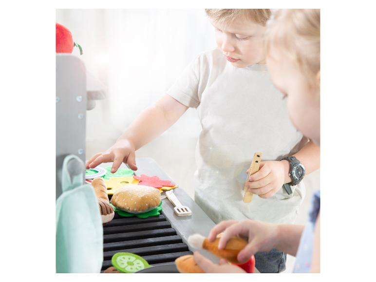 Kinderen spelen met een speelgoedbarbecue en vilten eten, waaronder een hamburger en groenten.