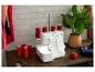 Witte naaimachine met rode draden op een houten tafel, naast een plant en accessoires.