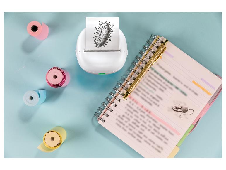 Witte miniprinter met bacterieprint, notitieboekje en pen op blauwe achtergrond.