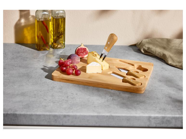 Houten kaasplank met kazen, vijgen, druiven en messen op een aanrecht.