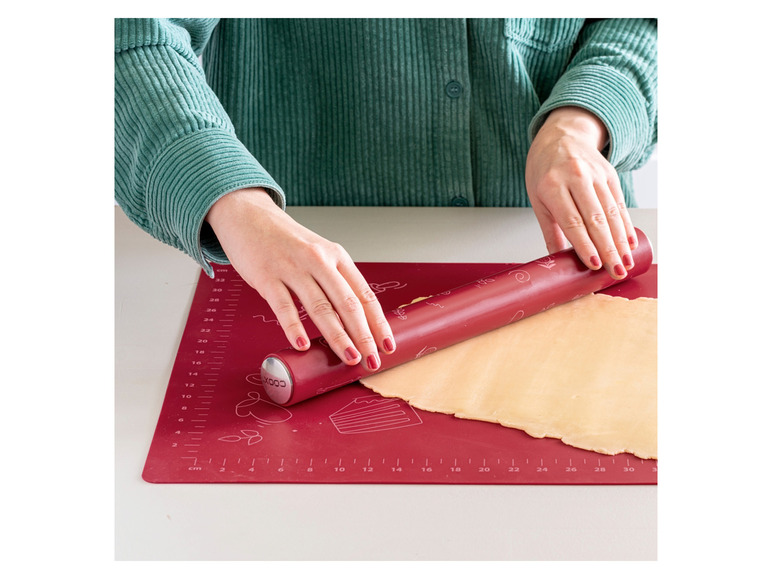 Een rood deegroller op een rode bakmat met een deeg er op.