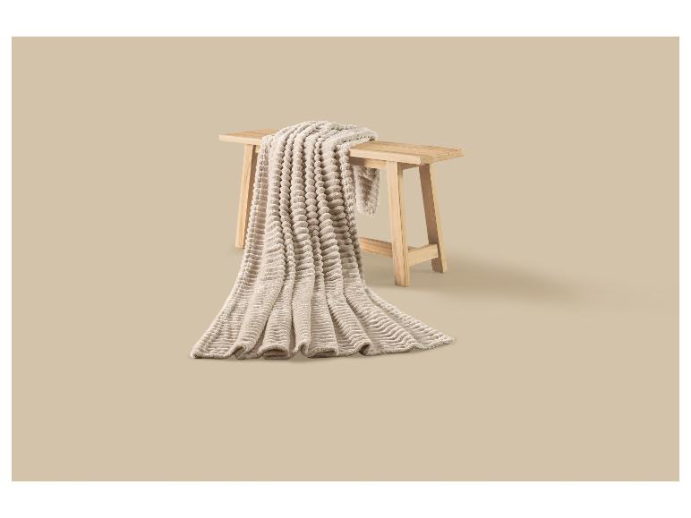 Beige, zachte deken met bubbeltextuur gedrapeerd over een houten bankje.