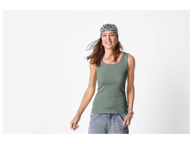 Vrouw in een groene geribbelde tanktop, denim shorts en een bandana met patroon, lachend.