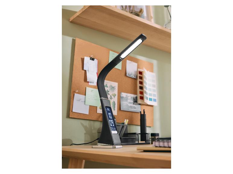 Zwarte LED-bureaulamp met digitaal display op een houten bureau met kurkbord.