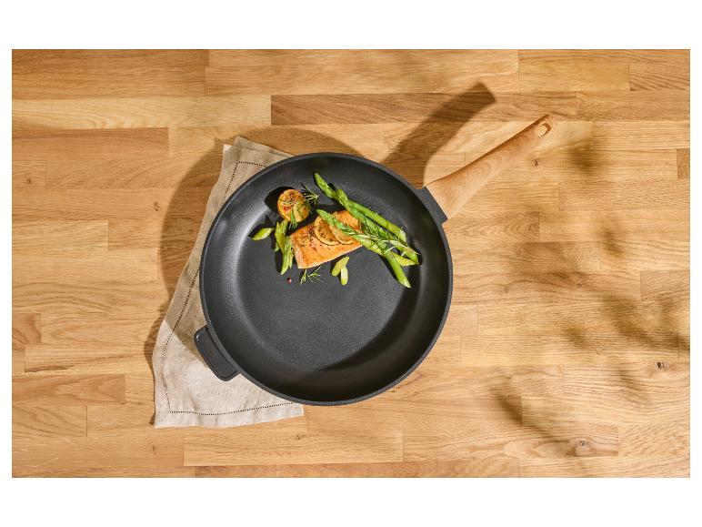 Koekenpan met zalm, asperges en citroen op een houten tafel.