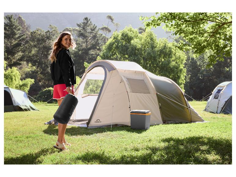 Vrouw met slaapmat voor een campingtent en koelbox in de natuur.