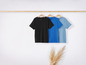 Drie T-shirts, zwart, donkerblauw en lichtblauw, hangen aan een houten hanger.