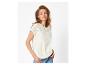 Vrouw in een witte geborduurde blouse en jeans, poserend tegen een witte achtergrond.