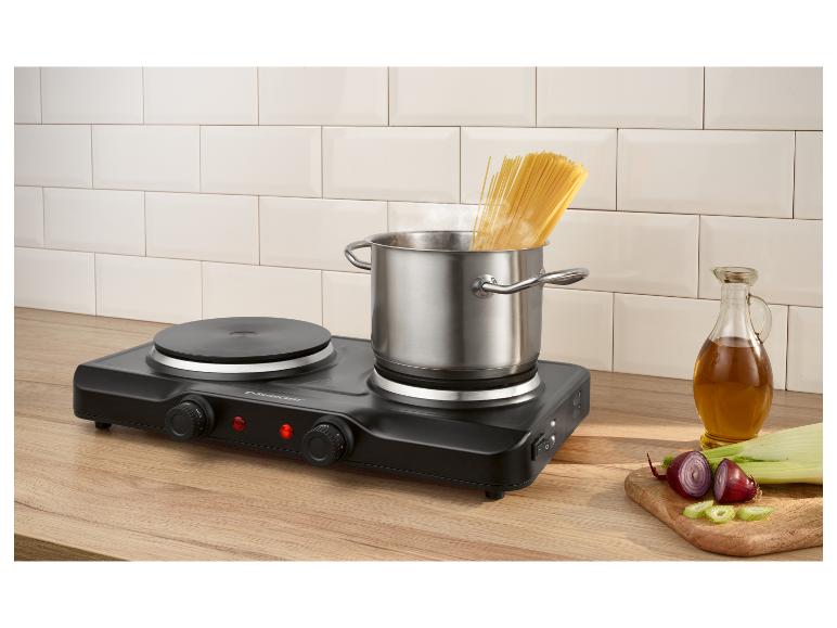 Draagbare elektrische kookplaat met een pan kokende spaghetti, olie en gesneden groenten.