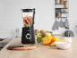 Zwarte blender met fruit (appels, bananen, sinaasappels, kiwi's) op een houten keukentafel.