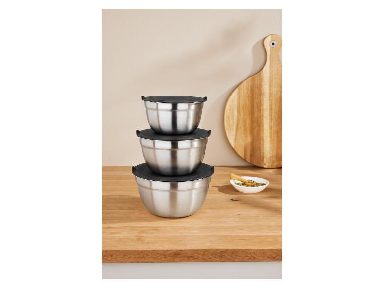Drie gestapelde roestvrijstalen mengkommen met zwarte deksels op een houten tafel.