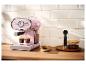 Roze espressomachine maakt koffie, met koekjes en koffiebonen op een houten aanrecht.