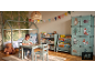 Kind tekent aan tafel in bos-thema kinderkamer met bed, boekenkasten en kledingkast.