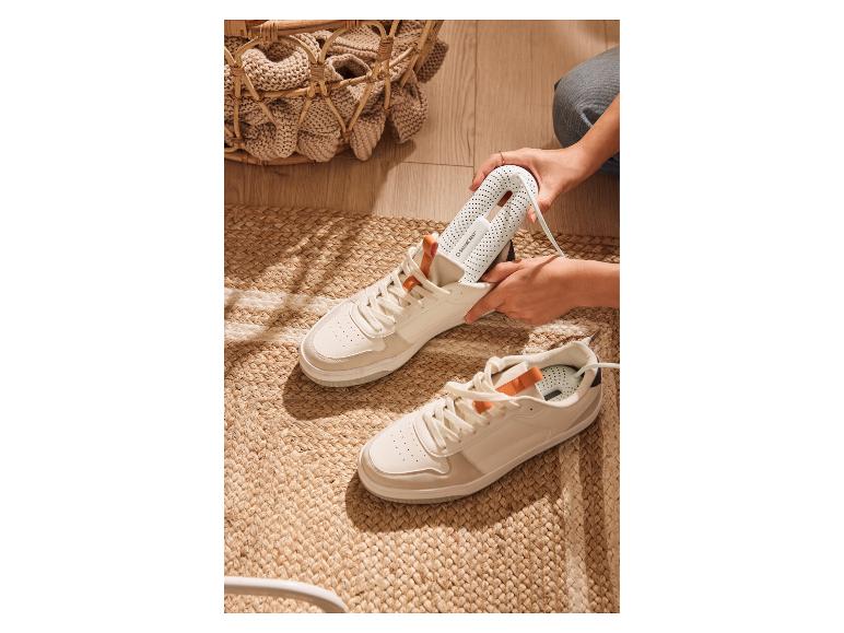 Een persoon steekt een witte schoendroger in een witte sneaker op een geweven vloerkleed.