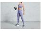 Een vrouw in paarse sportkleding houdt een kettlebell vast.